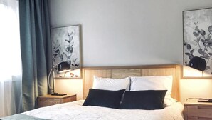 A modern bedroom with a large bed, wooden headboard, two bedside tables with lamps, and artwork on the walls.