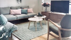 A modern living room with a grey sofa, a round coffee table, a wooden chair, a TV, and a ceiling fan.