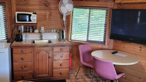 A cozy cabin interior with a wooden ceiling, a kitchenette, a dining area with a table and chairs, and a large TV mounted on the wall.