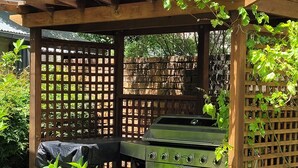 A wooden pergola with a built-in grill and potted plants.