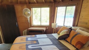 A wooden cabin bedroom with a bed, a desk, and a fan.