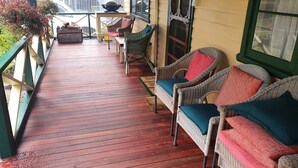 Una terraza de madera con mobiliario de mimbre y vistas a un patio cercado.