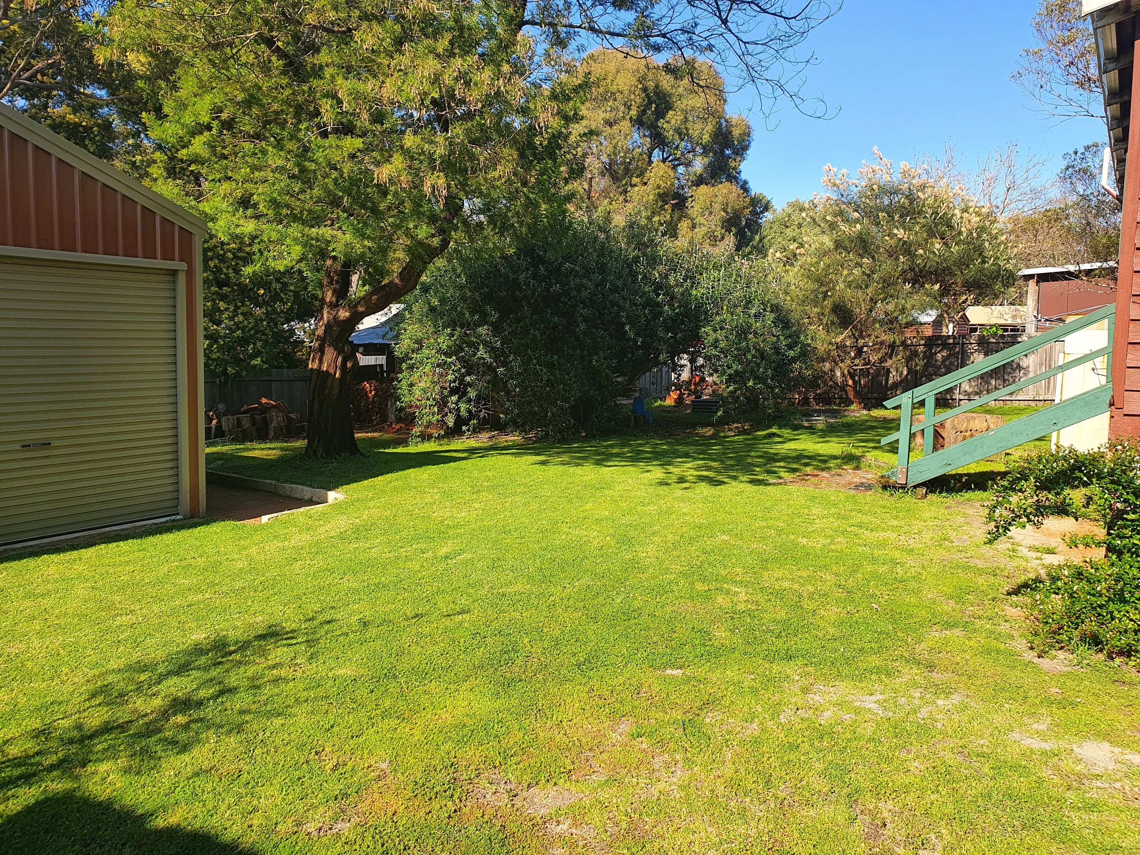 A well-maintained yard with a large tree, a wooden staircase, and a garage door.