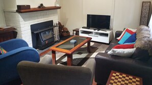 Una sala de estar con chimenea, un televisor sobre un mueble bajo, una mesa de centro y un sofá con un cojín de cuadros.