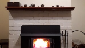Una chimenea con un cuadro encima, un repisa decorada con piñas y dos vasos sobre la repisa.