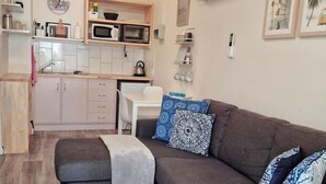 Ein gemütlicher, kompakter Wohnbereich mit Sofa, kleinem Tisch, Mikrowelle und Küchenzeile.