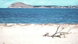 Ein Strand mit sandigem Ufer und einer kleinen Erhebung in der Ferne.
