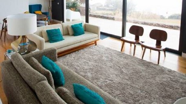 A modern living room with a high ceiling, large windows, and a view of the outdoors.