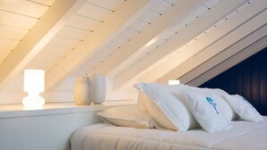 A bedroom with a sloped ceiling, a bed with white bedding, and a nightstand with a lamp and a vase.