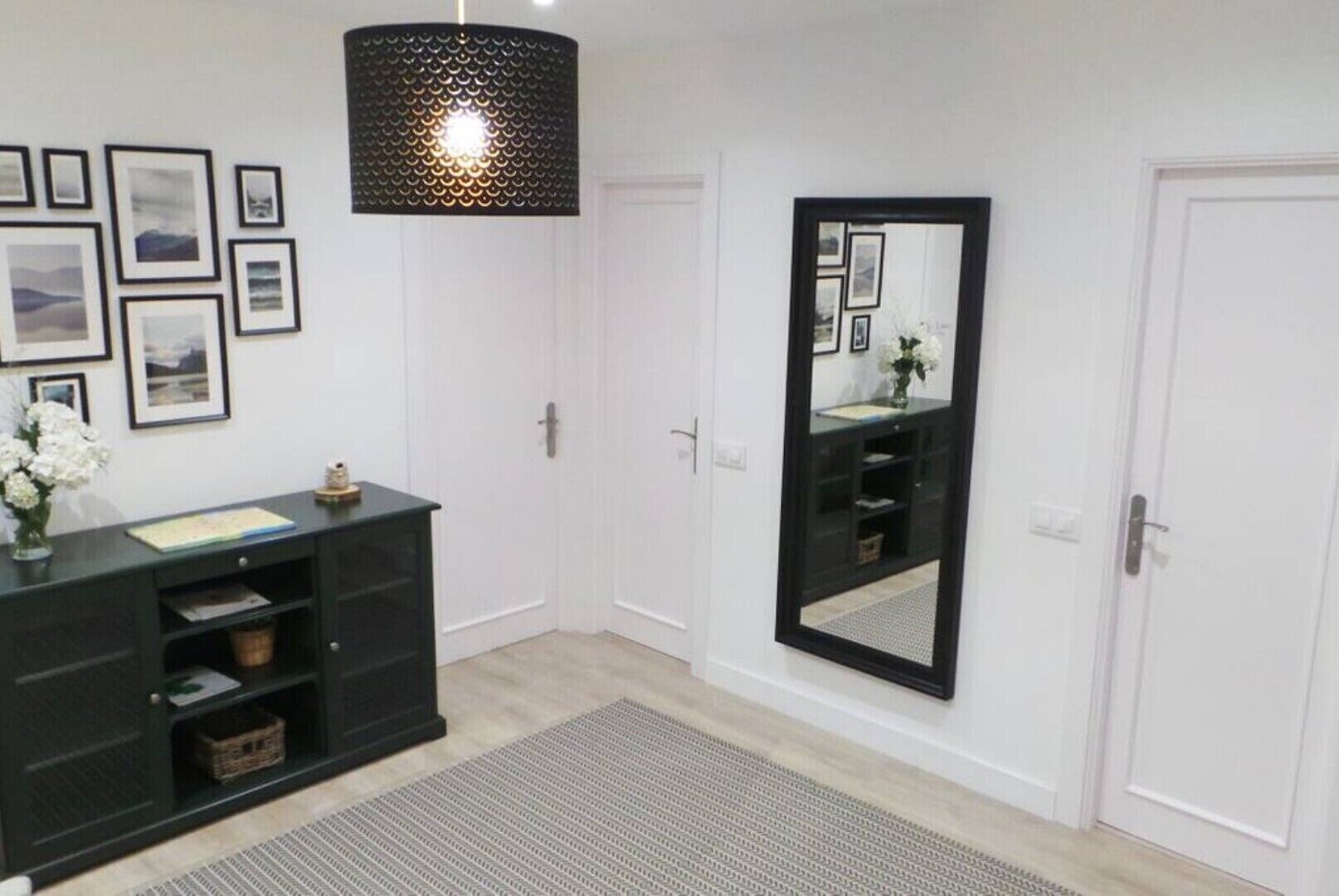 Una habitación con un escritorio oscuro, un espejo grande y cuadros enmarcados en la pared.