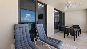 A balcony with two lounge chairs, a table, and a ceiling fan.