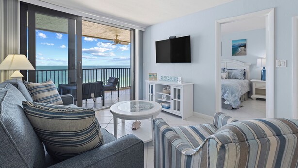 A modern living room with a large window, a round glass table, striped sofas, and a white cabinet.