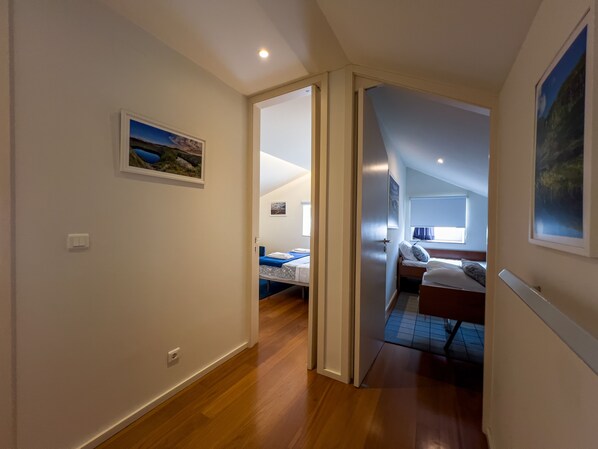 A hallway leading to a bedroom with a bed, a desk, and a window.