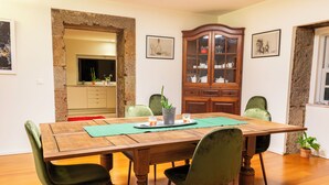 A dining area with a wooden table, green upholstered chairs, a cabinet with glass doors, and a kitchen visible through an archway. - Casa do Becco - with breathtaking views of the ocean and the historic center (Angra do Heroísmo)