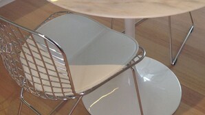 A modern kitchen with a round marble table, two wireframe chairs, and a built-in oven.