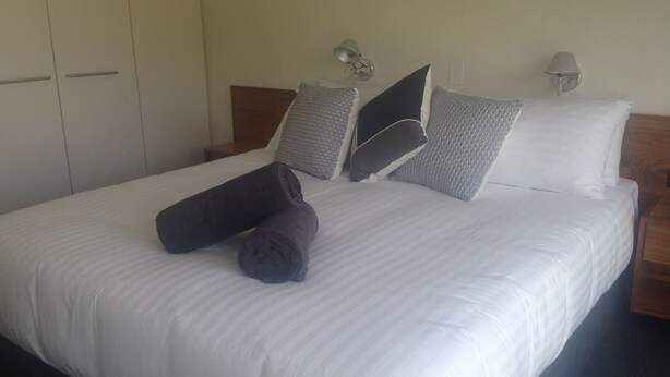A neatly made bed with white linens, a dark gray throw blanket, and several pillows in shades of gray and white.