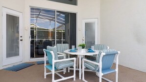 En terrasse med et hvidt bord og stole, en skydedør og en lille potteplante.