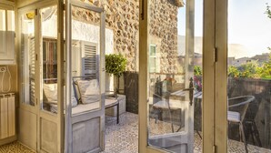 A sunlit patio with a stone wall, a glass door, and a seating area with a table and chairs. - Stunning, romantic 1 Bedroom Property With Terrace (Fornalutx)