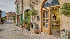 A stone building with arched windows and a wooden door, potted plants, and a cobblestone street. - Stunning, romantic 1 Bedroom Property With Terrace (Fornalutx)
