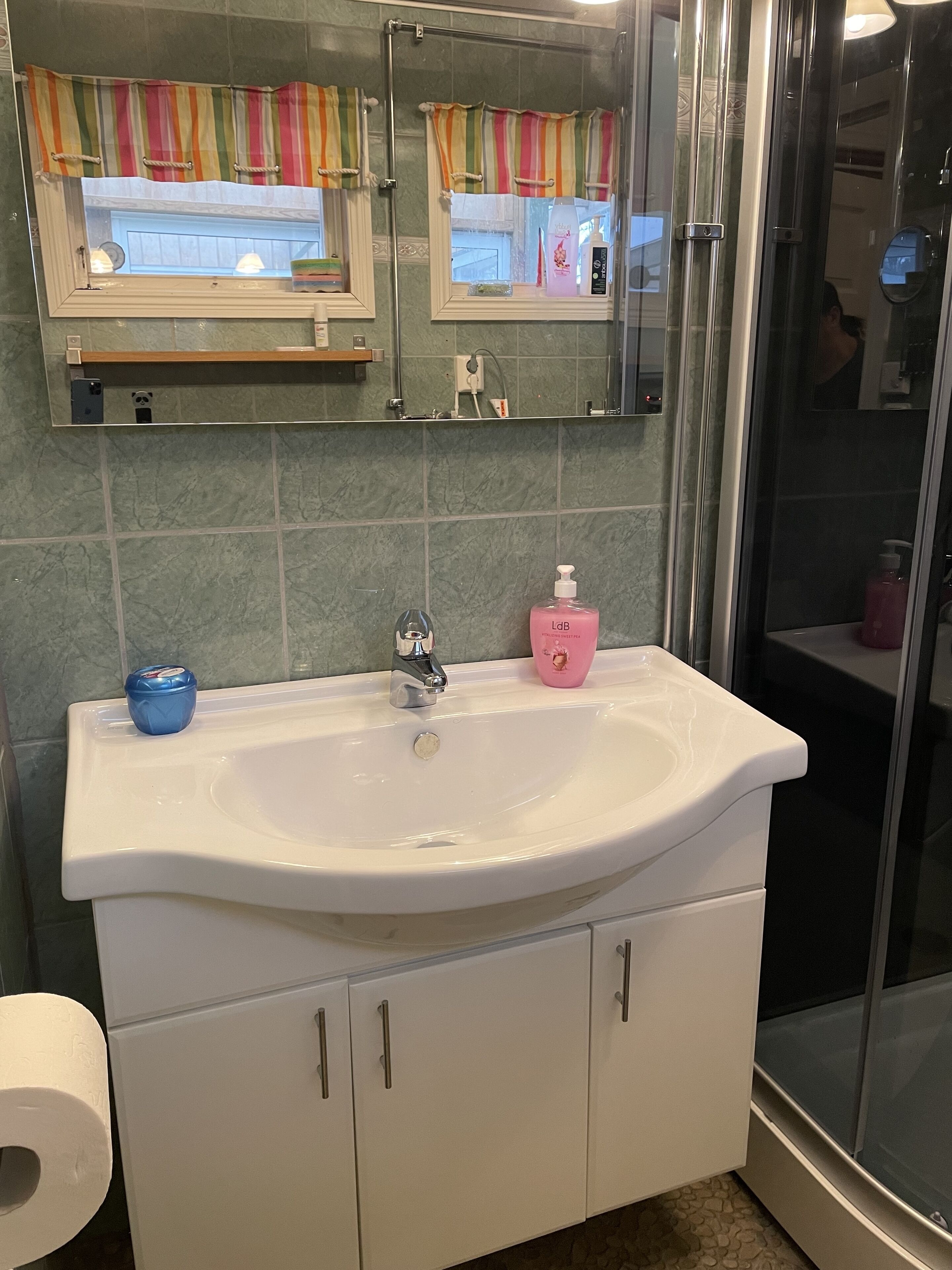 Un bagno con lavandino bianco, uno specchio e zona doccia.