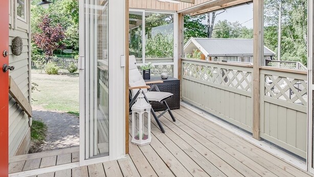 Une terrasse en bois avec une chaise blanche et une lanterne, une clôture en bois et une vue sur une maison et des arbres.