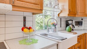 Une cuisine moderne avec des meubles en bois, un plan de travail blanc, un évier, un four à micro-ondes et un panier à fruits.