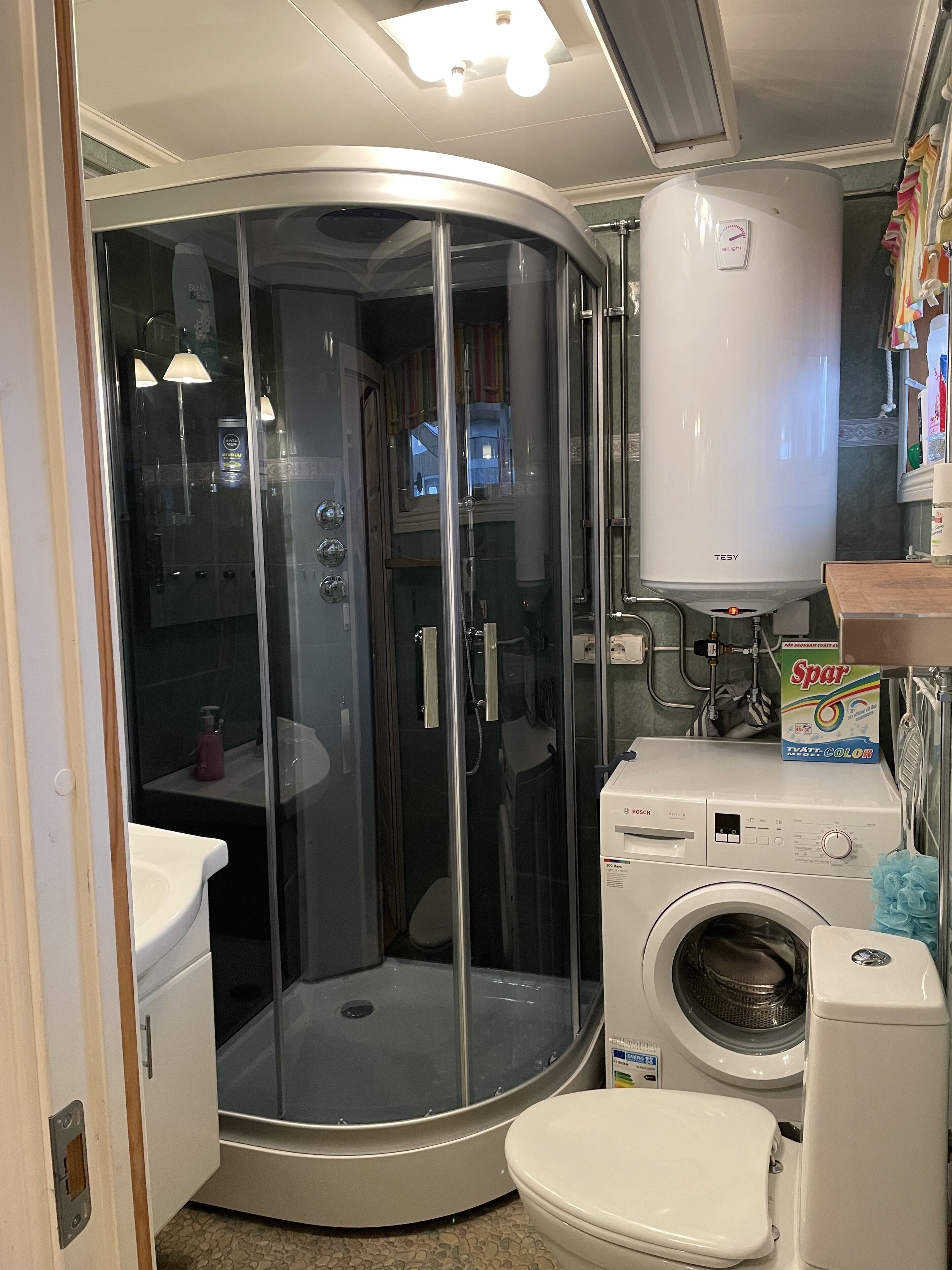 Een kleine badkamer met een douchecabine, een Bosch wasmachine en een boiler.
