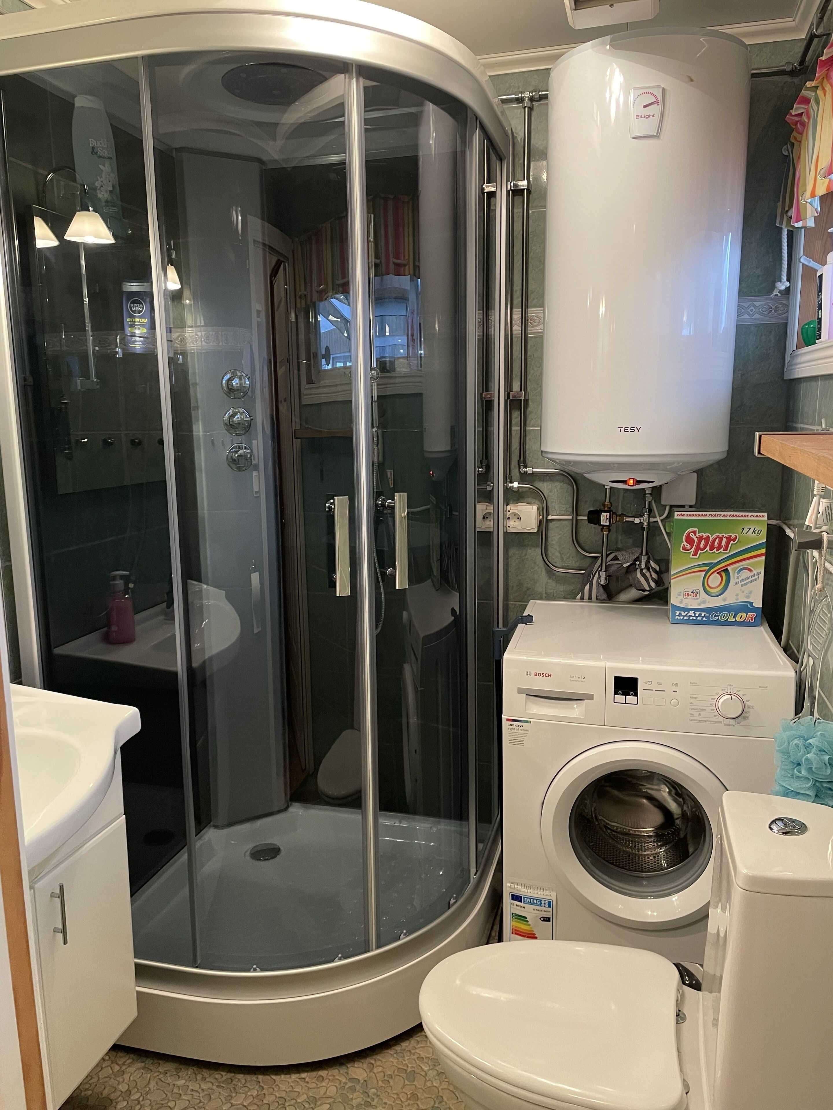 A compact bathroom with a glass-enclosed shower, a Bosch washing machine, and a toilet.