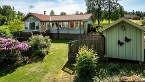 Une maison à deux étages avec un porche, une cour clôturée et un petit abri de jardin.