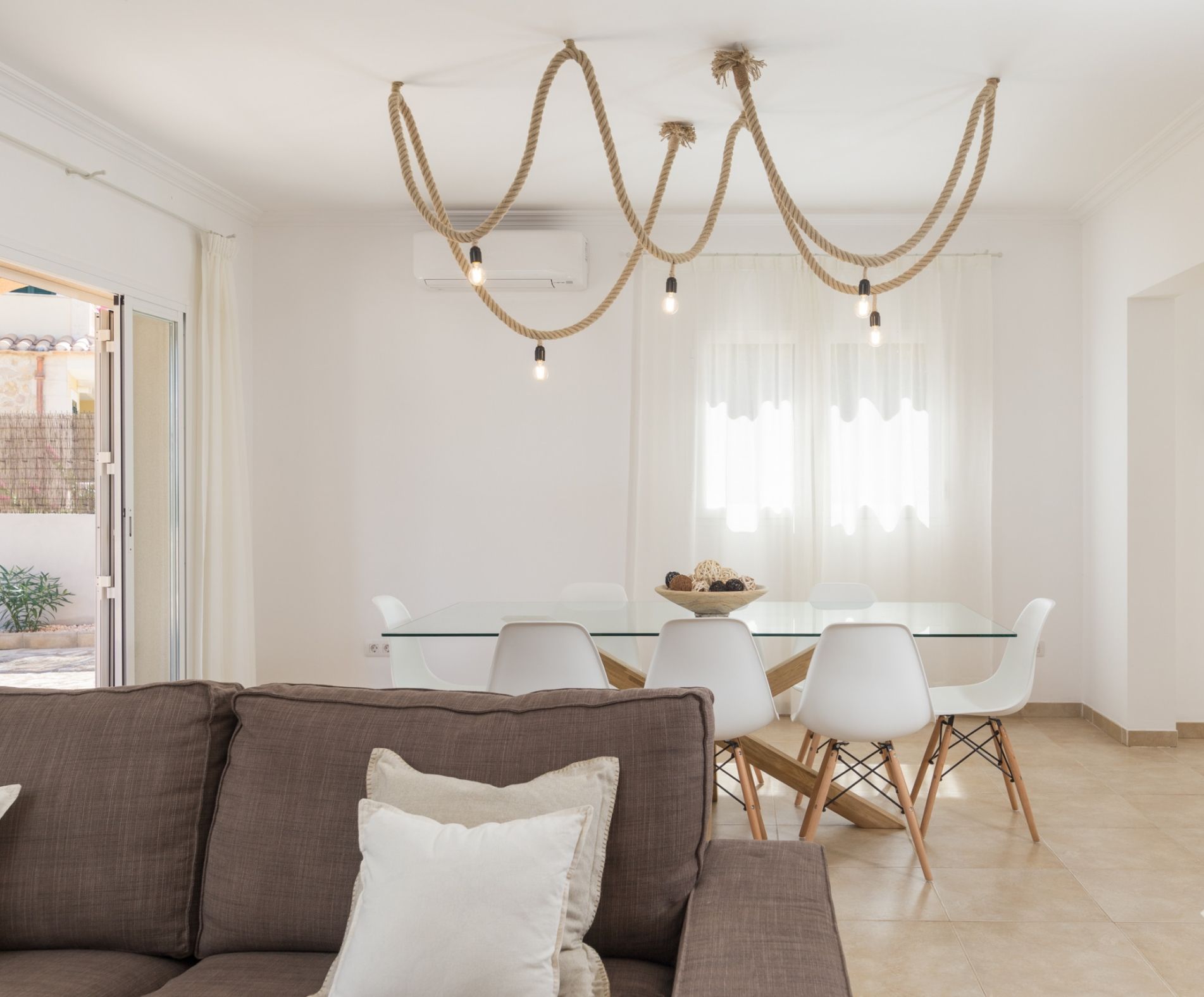 A modern dining area with a glass table, white chairs, and a chandelier.