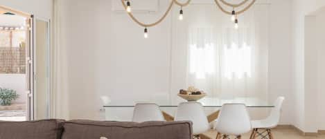 A modern dining area with a glass table, white chairs, and a chandelier.
