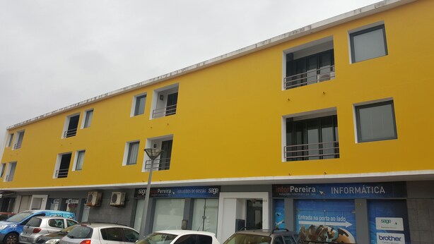 Un edificio amarillo con múltiples ventanas y unidades de aire acondicionado. Varios coches están estacionados adelante.