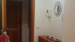 Un pasillo con una puerta de madera, un extintor, un armario de madera y un teléfono instalado en la pared.