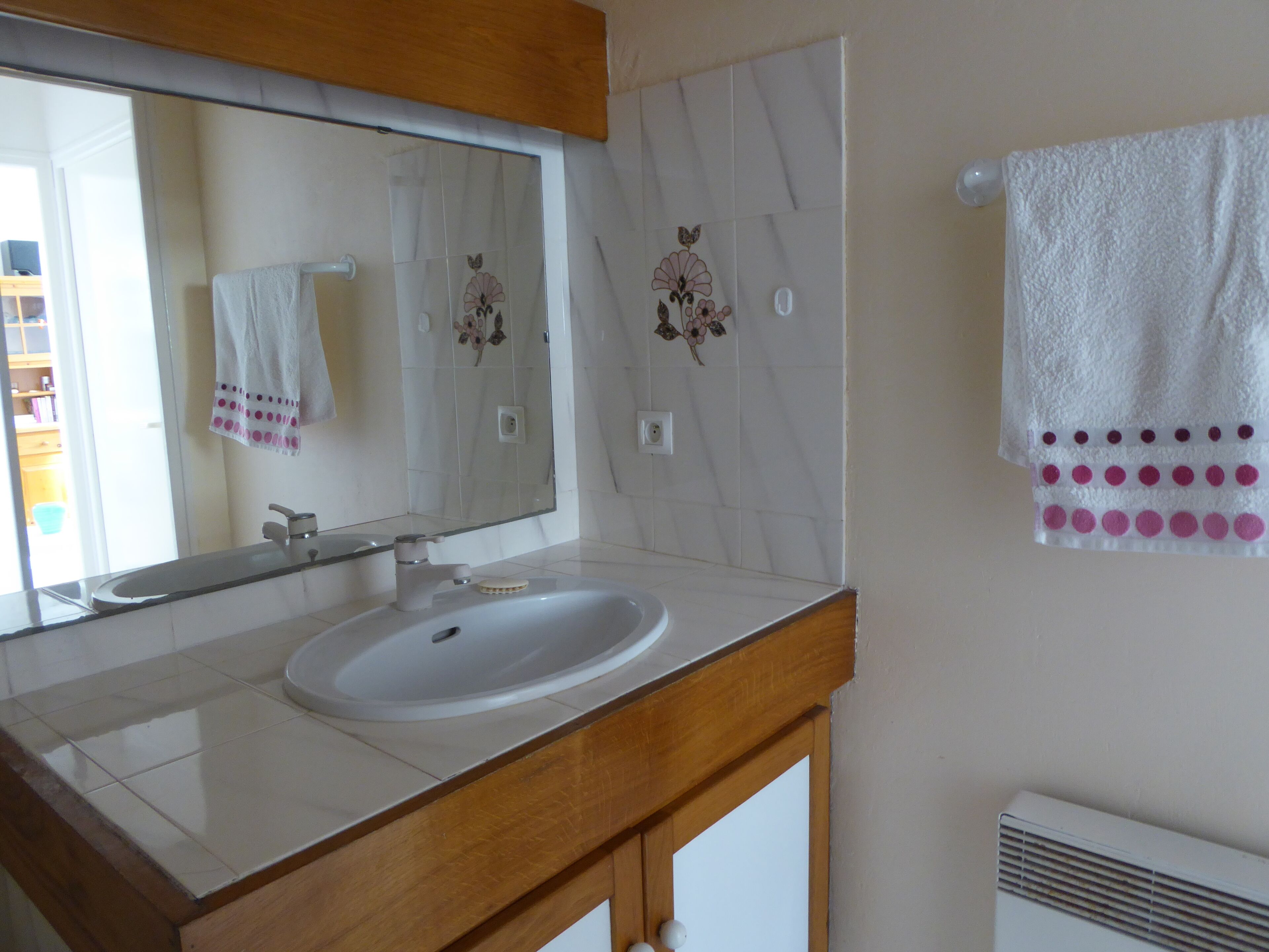 A bathroom with a white sink, a mirror, and a towel rack with a white towel and a pink towel.