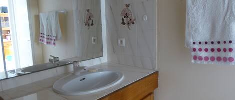 A bathroom with a white sink, a mirror, and a towel rack with a white towel and a pink towel.
