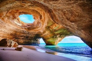 Une formation rocheuse naturelle dotée d’une ouverture circulaire, une plage de sable et l’océan.