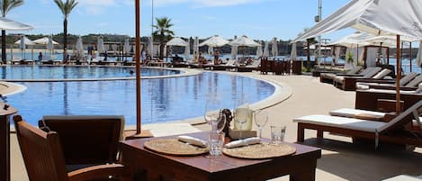 A poolside area with lounge chairs, umbrellas, and a table with glasses and a bottle.