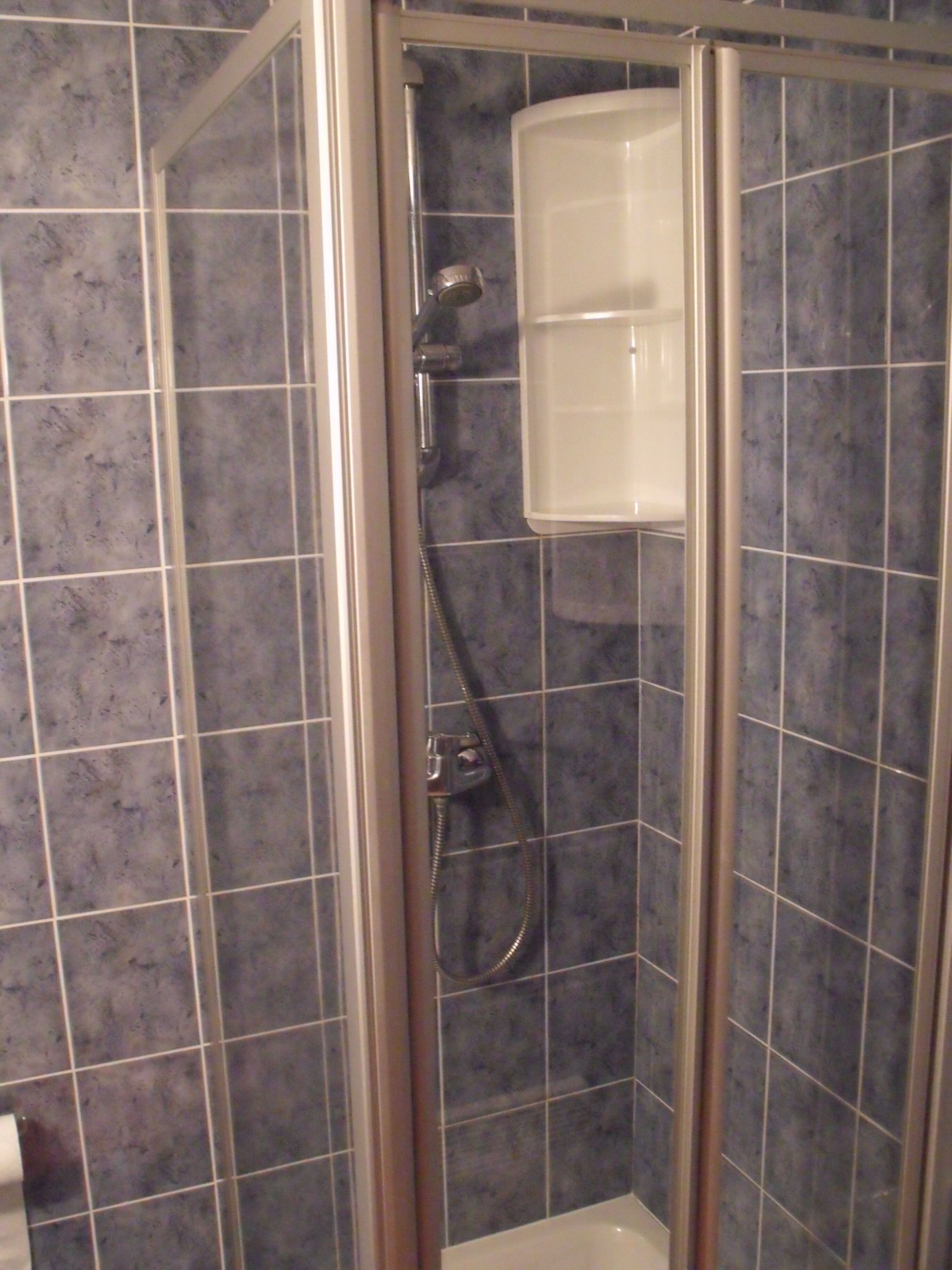 Un cerramiento de ducha con puerta de vidrio, un cabezal de ducha de mano y un grifo empotrado en la pared.