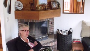 Ein Zimmer mit Kamin, einem aufgehängten Hirschgeweih und einer Person, die in einem Sessel sitzt.