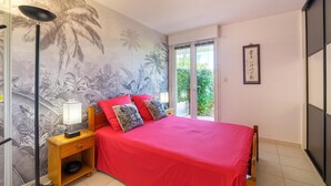 A bedroom with a red bedspread, a nightstand with a lamp, and a wall with a tropical mural. - Gorgeous apartment in ST Raphael with outdoor swimming pool (ST Raphael)