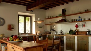 Une cuisine avec des meubles de rangement en bois, un îlot central sur lequel se trouve un saladier rempli de fruits, et un luminaire suspendu.