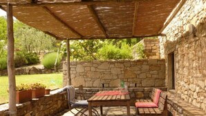 Une terrasse extérieure avec des murs en pierre, une table en bois et deux bancs en bois.