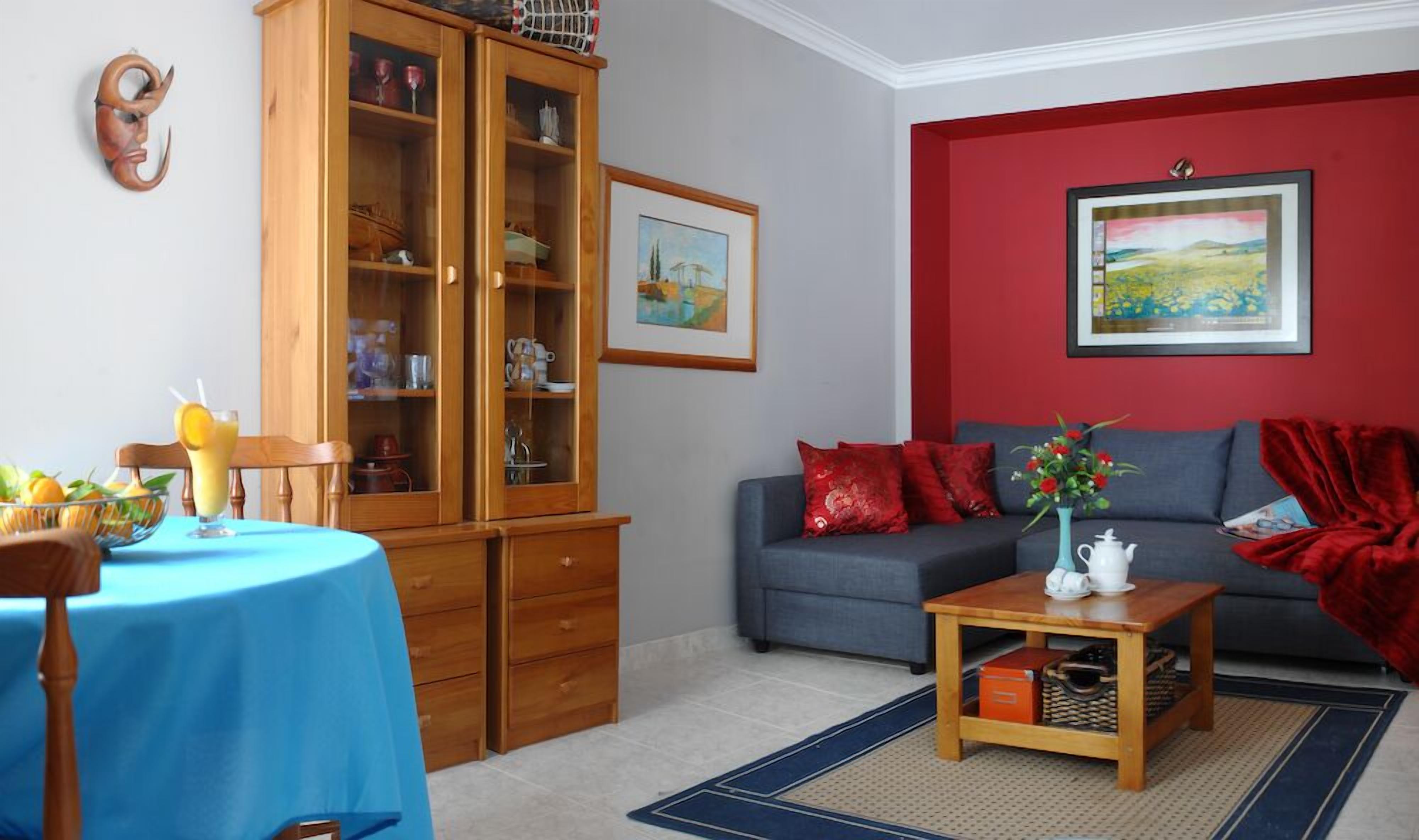 Un soggiorno con un tavolo blu, un divano grigio, un mobile in legno e una parete rossa con un quadro.