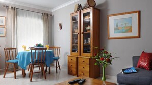 A dining area with a blue tablecloth, wooden chairs, a cabinet, and a vase with flowers.