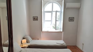 A small, clean room with two beds, a window, and a nightstand with a lamp. - Carolina M Apt in front of Metro (Porto)