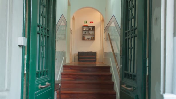 A staircase with wooden steps and green doors, leading to a landing with a shelf of items. - Carolina M Apt in front of Metro (Porto)