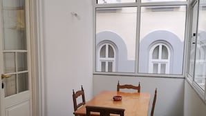 A room with a wooden table and chairs, a door, and a window with a view of another building. - Carolina M Apt in front of Metro (Porto)