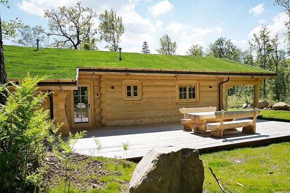 A log cabin with a deck and a bench, surrounded by greenery and trees. - Beautiful luxury log cabin. Two private terrasses. Open fireplace. Pet friendly (Växtorp)