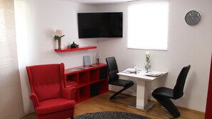 A modern room with a red armchair, a white desk with two black chairs, a flat-screen TV, and a clock on the wall. - Lake Constance, Friedrichshafen, central location, 2 people (Friedrichshafen)