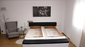 A modern bedroom with a large bed, a checkered armchair, a bedside table, and a wall-mounted artwork. - Lake Constance, Friedrichshafen, central location, 2 people (Friedrichshafen)